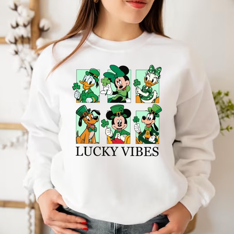 May include: White sweatshirt with a green, white, and black graphic of Mickey Mouse, Minnie Mouse, Donald Duck, Goofy, and Pluto wearing green hats and holding shamrocks. The text "LUCKY VIBES" is printed below the graphic.