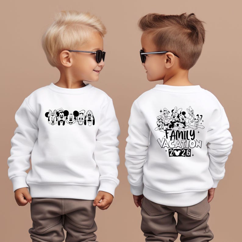 May include: White sweatshirt featuring a black and white graphic of Disney characters on the front and back. The front displays character faces, while the back says "Family Vacation 2026". The sweatshirt is worn by a child.