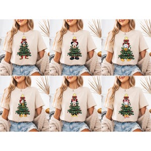 May include: Beige t-shirts featuring Christmas tree designs with cartoon characters. Each shirt showcases a different character, including Mickey Mouse, Minnie Mouse, Donald Duck, and Goofy, all dressed in festive attire. The trees are decorated with ornaments and topped with a star.