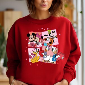 May include: Red sweatshirt with a Valentine's Day design featuring Mickey Mouse, Minnie Mouse, Donald Duck, Goofy, and Pluto. The characters are holding hearts and surrounded by pink hearts.