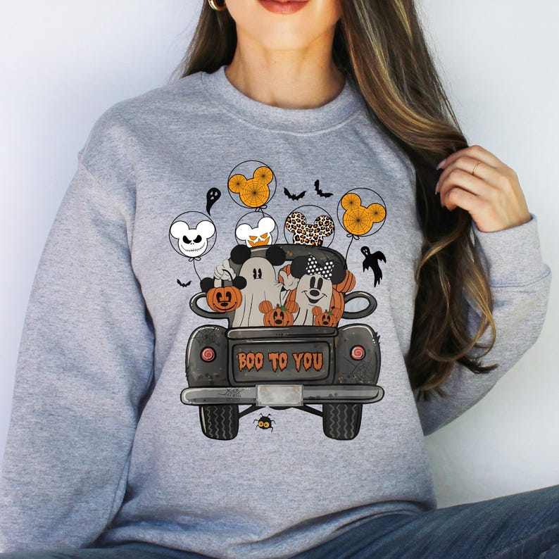 Peut inclure: Un sweat-shirt gris avec un motif sur le th&egrave;me d'Halloween repr&eacute;sentant Mickey Mouse et ses amis dans un pick-up avec des citrouilles et des ballons. Le texte "BOO TO YOU" est imprim&eacute; &agrave; l'arri&egrave;re du camion.