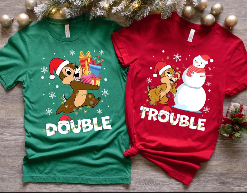 Puede incluir: Dos camisetas con tem&aacute;tica navide&ntilde;a con un chipmunk de dibujos animados que lleva un gorro de Pap&aacute; Noel. La camiseta verde dice "Double Trouble" y la camiseta roja dice "Trouble".