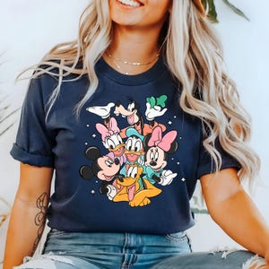 May include: A navy blue t-shirt with a graphic print of Mickey Mouse, Minnie Mouse, Donald Duck, Goofy, and Pluto. The characters are arranged in a playful cluster, with Mickey Mouse and Minnie Mouse in the foreground.