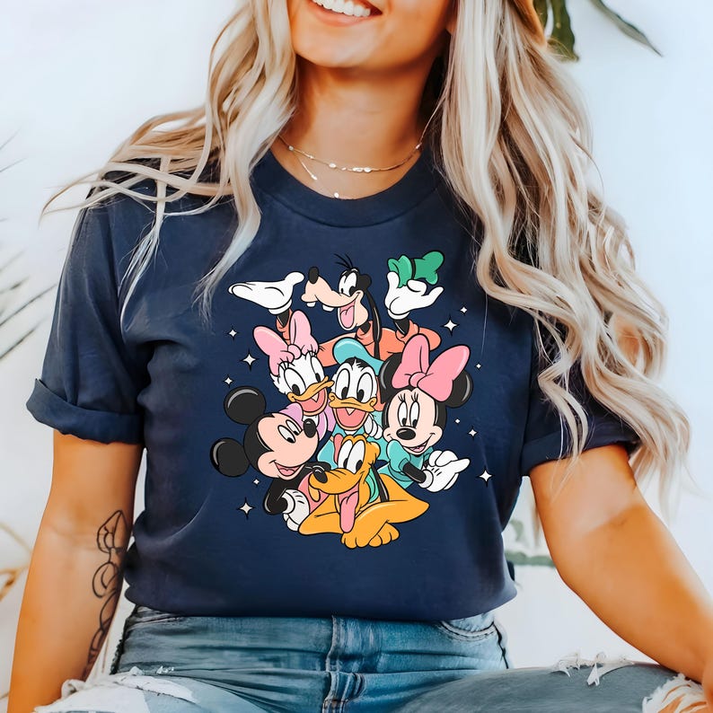 May include: A navy blue t-shirt with a graphic print of Mickey Mouse, Minnie Mouse, Donald Duck, Goofy, and Pluto. The characters are arranged in a playful cluster, with Mickey Mouse and Minnie Mouse in the foreground.