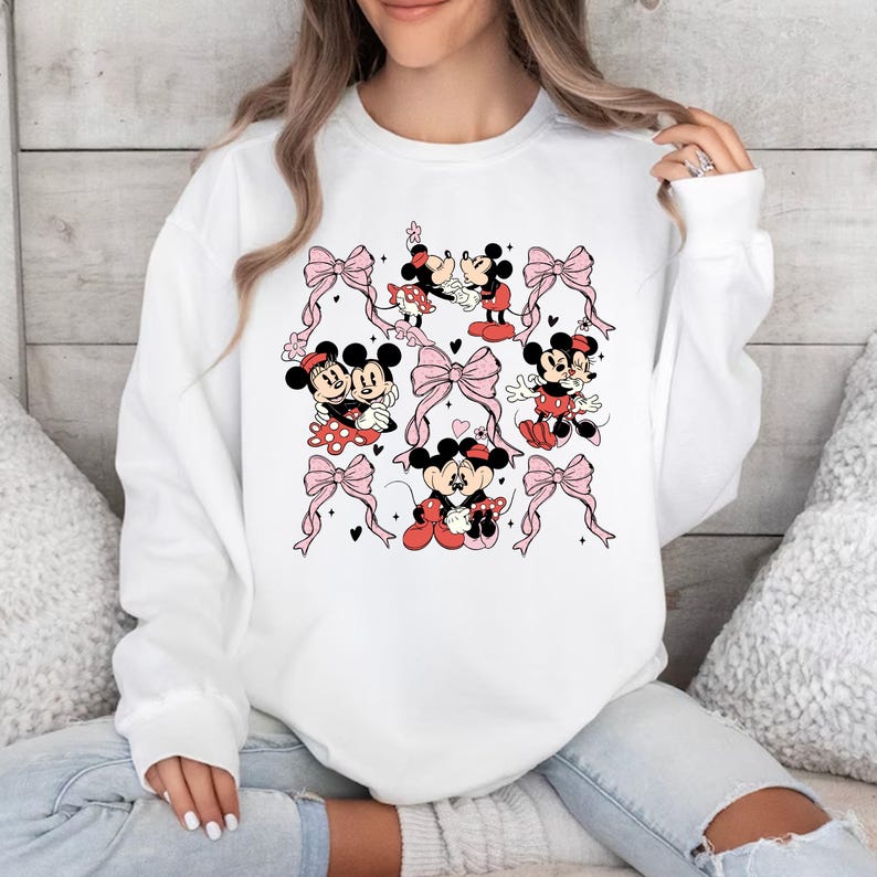 May include: White sweatshirt with a graphic print of Mickey Mouse and Minnie Mouse in various poses. The print features pink bows and hearts.
