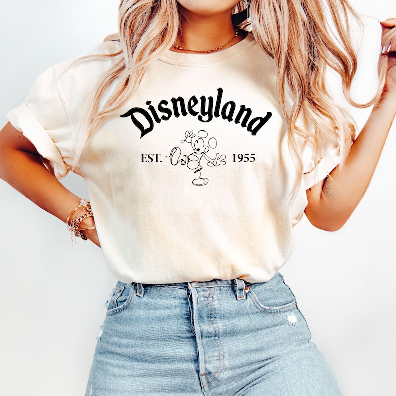 May include: A white t-shirt with black text that reads "Disneyland Est. 1955" and a black and white illustration of Mickey Mouse.