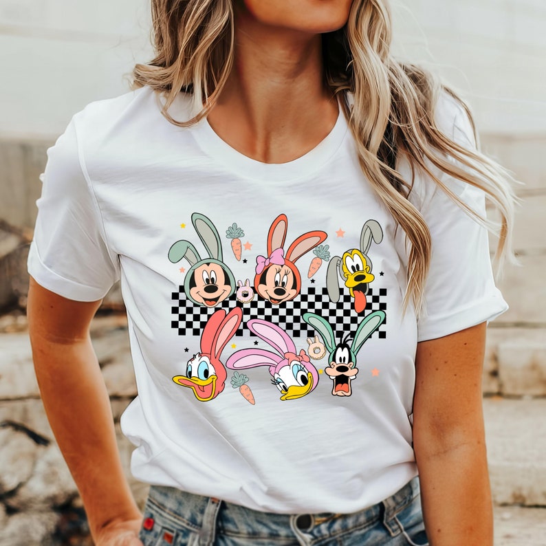 May include: White t-shirt with a colorful graphic print of cartoon characters wearing bunny ears. The characters include Mickey Mouse, Minnie Mouse, Donald Duck, Goofy, and Pluto.