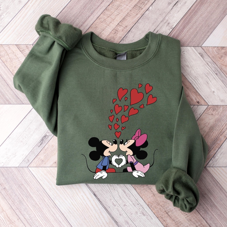 May include: Green sweatshirt with a graphic of Mickey Mouse and Minnie Mouse kissing. Red hearts are floating above them.