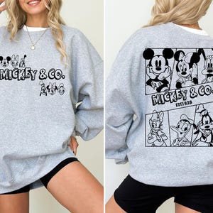 May include: A gray sweatshirt with a black print of Mickey Mouse and friends. The print includes the text "Mickey & Co. Est. 1928".
