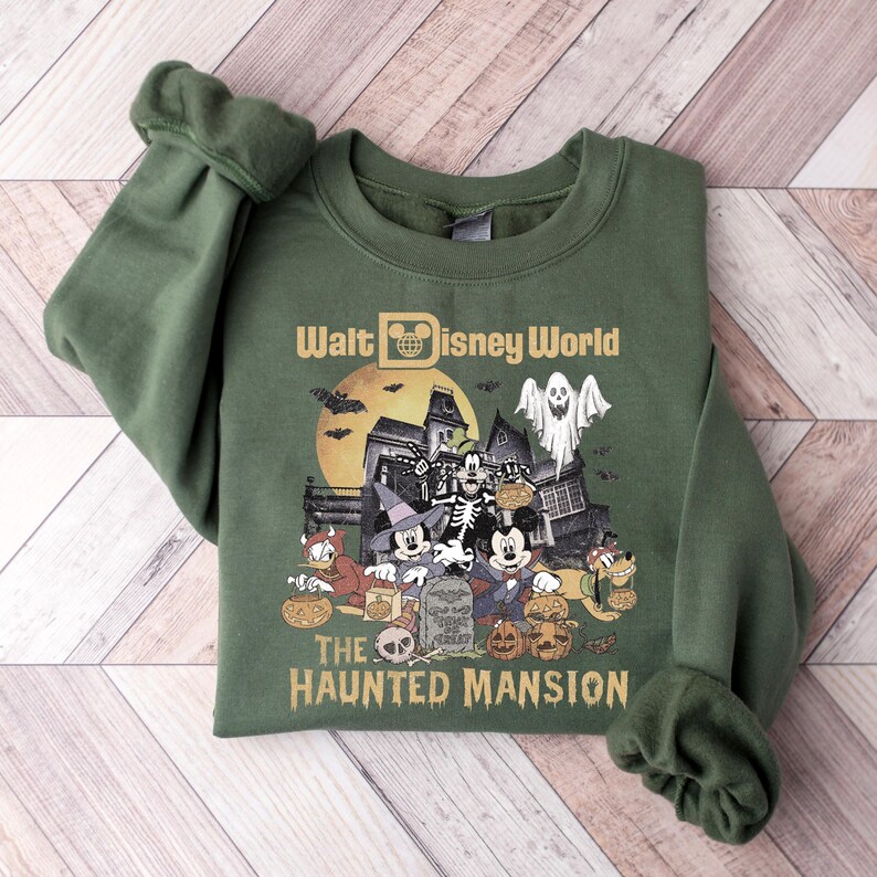 May include: A green sweatshirt with a graphic of Mickey Mouse and friends in front of the Haunted Mansion at Walt Disney World. The text "Walt Disney World" and "The Haunted Mansion" are printed on the sweatshirt.