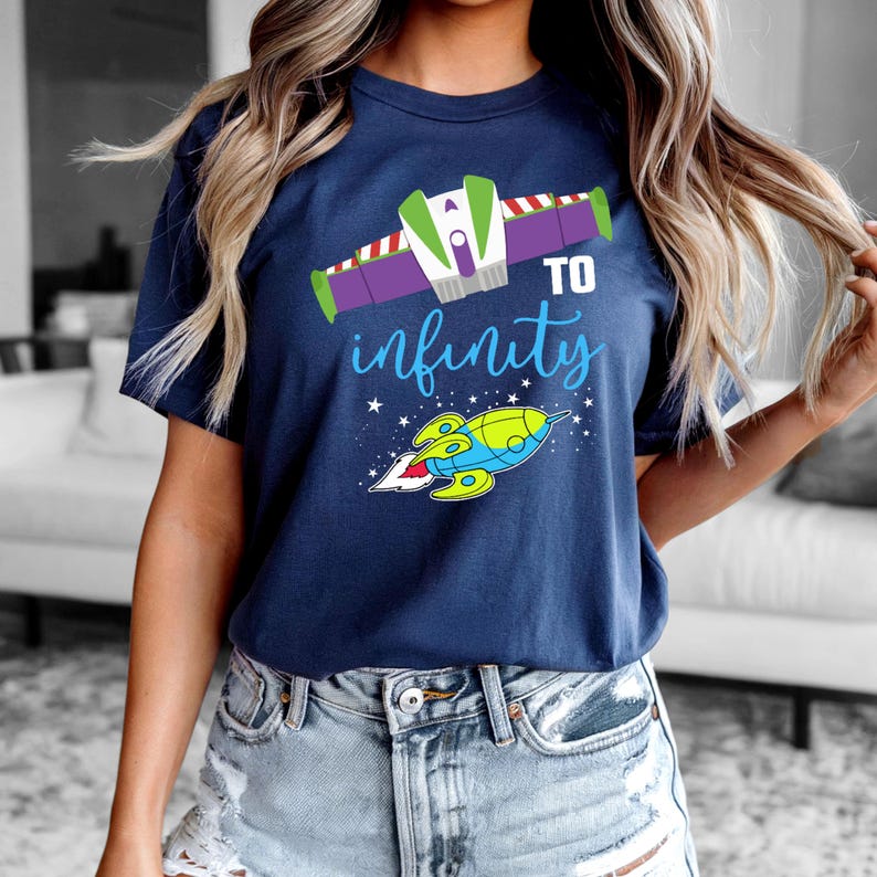Peut inclure: Un t-shirt bleu marine avec un graphique de vaisseau spatial et le texte "To infinity" en lettres blanches. Le vaisseau spatial est vert, jaune et bleu.
