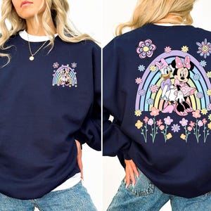 May include: A navy blue sweatshirt with a rainbow and flower design featuring Minnie Mouse and Daisy Duck. The design is on the back of the sweatshirt. The front of the sweatshirt has a smaller design of Minnie Mouse and Daisy Duck.