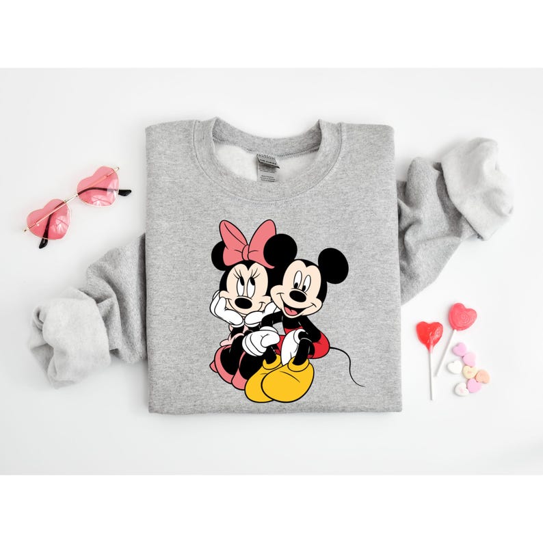 May include: A gray sweatshirt with a graphic print of Mickey Mouse and Minnie Mouse holding hands. The print is in black, red, and yellow.