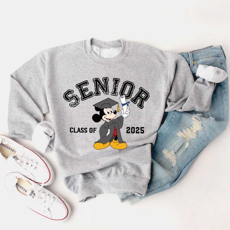 Op de afbeelding: Grijs sweatshirt met een zwart-witte cartoon van Mickey Mouse die een afstudeerpet draagt en een diploma vasthoudt. De tekst "SENIOR CLASS OF 2025" is op het sweatshirt gedrukt.