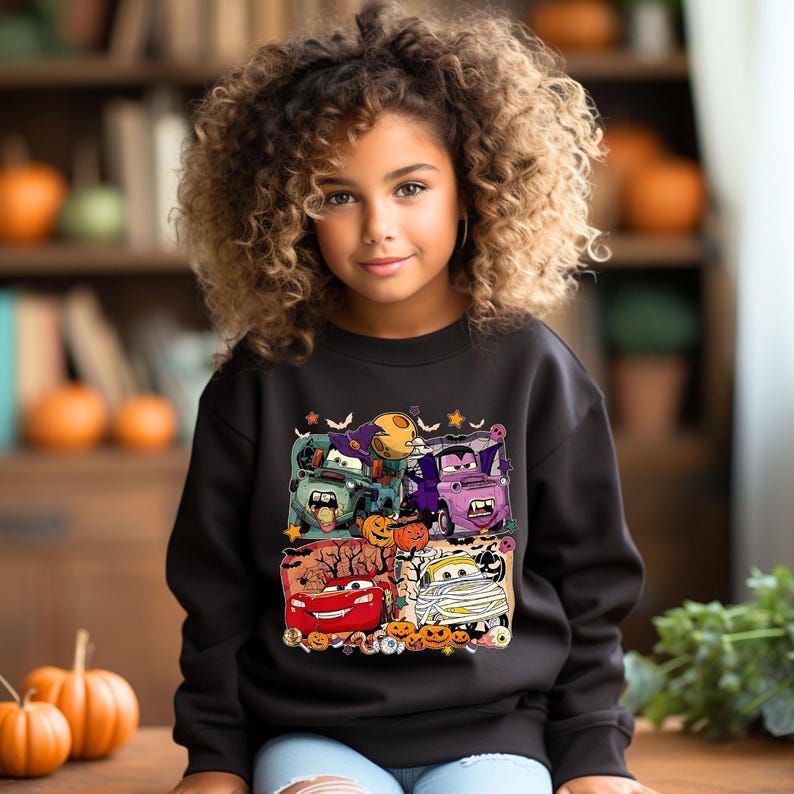 May include: A black sweatshirt with a Halloween-themed graphic featuring cartoon cars dressed as monsters. The cars are surrounded by pumpkins, bats, and other Halloween decorations.