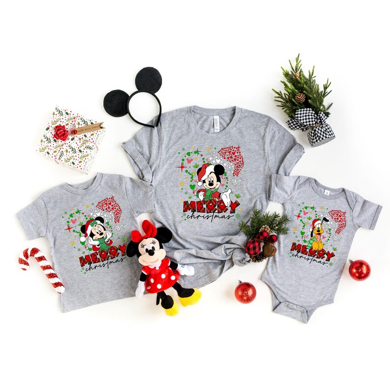 May include: Three grey t-shirts with a Christmas theme featuring Mickey Mouse, Minnie Mouse, and Goofy. The shirts have the text "Merry Christmas" on them.