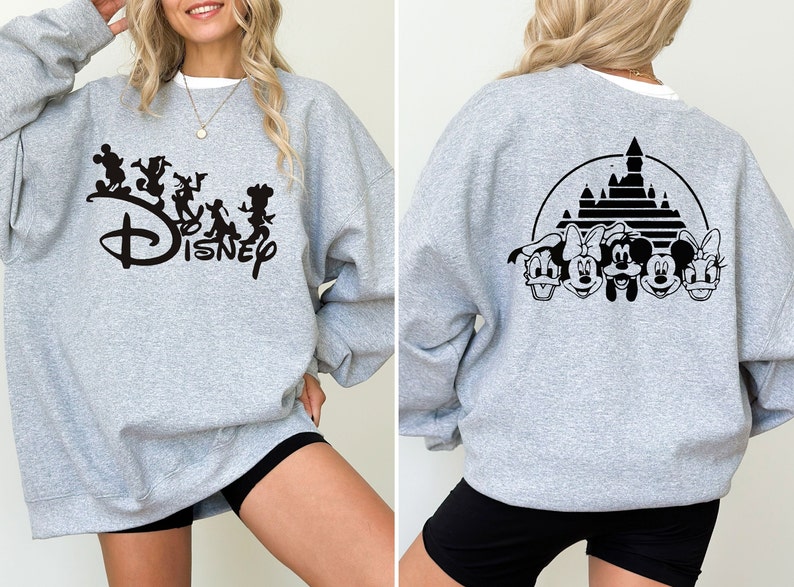 Puede incluir: Sudadera gris con un logotipo de Disney negro y personajes en la parte delantera y una silueta negra del castillo de Disney y personajes en la parte posterior.