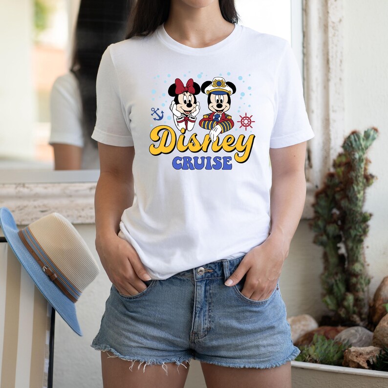 May include: White t-shirt with a graphic of Mickey Mouse and Minnie Mouse dressed in nautical outfits. The text "Disney Cruise" is printed in yellow on the shirt.