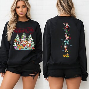 Puede incluir: Sudadera negra con dise&ntilde;o navide&ntilde;o. La parte delantera muestra a Mickey Mouse, Donald Duck y amigos con regalos y &aacute;rboles de Navidad, con el texto "The Most Wonderful Time of the Year". La parte trasera presenta personajes de Disney.