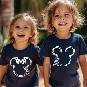 May include: Two children wearing navy blue t-shirts with white outlines of Mickey Mouse and Minnie Mouse heads. The girl's shirt has a black and white polka dot bow on Minnie Mouse's head.