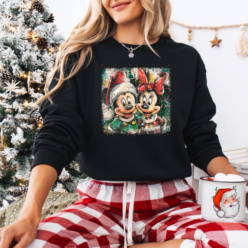 May include: Black sweatshirt featuring a colorful graphic of Mickey and Minnie Mouse in Christmas attire. Mickey wears a Santa hat and green jacket, while Minnie sports a red bow and jacket. The sweatshirt is paired with red and white plaid pajama pants.