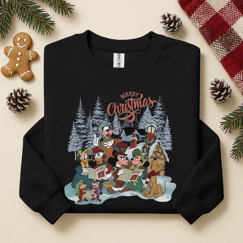 May include: Black crewneck sweatshirt featuring a festive scene with Disney characters singing carols in a snowy village. The words "Merry Christmas" are written in a decorative script above the characters. The sweatshirt is a Gildan brand.