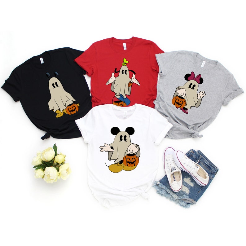 Pode incluir: Quatro camisetas de Halloween em preto, vermelho, branco e cinza. Cada camisa apresenta um personagem de desenho animado vestido como um fantasma segurando uma lanterna de ab&oacute;bora. Os personagens incluem Mickey Mouse, Minnie Mouse e Pateta.