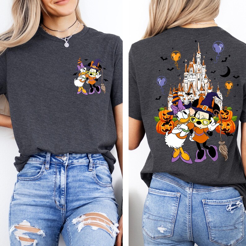 May include: Dark gray t-shirt featuring a Halloween-themed graphic of Minnie Mouse and Daisy Duck in witch costumes. The back of the shirt displays a castle, pumpkins, and bats. The shirt has a crew neck and short sleeves.
