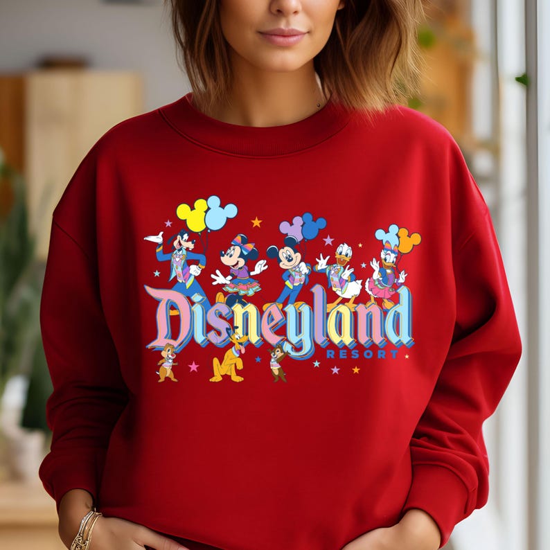 May include: Red sweatshirt with a colourful Disneyland graphic featuring Mickey Mouse, Minnie Mouse, Donald Duck, Goofy, and Pluto. The graphic includes the text "Disneyland Resort".
