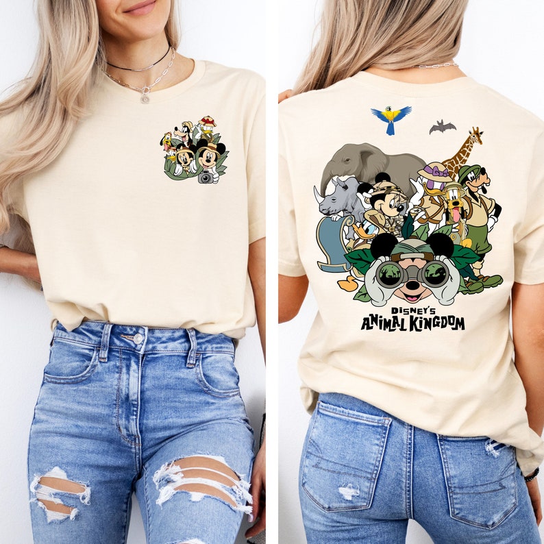 May include: A beige t-shirt with a graphic print of Mickey Mouse and friends in safari gear. The back of the shirt has a larger graphic of Mickey Mouse with binoculars and the text "Disney's Animal Kingdom".