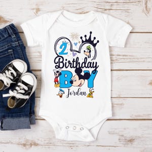 Op de afbeelding: Witte romper met een blauw Mickey Mouse-orenontwerp. Het ontwerp bevat Mickey Mouse, Donald Duck, Goofy en Pluto. De tekst op de romper luidt "2 Birthday Boy Jordan".
