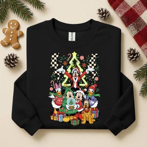 May include: Black sweatshirt featuring a festive graphic of Mickey Mouse and friends dressed for Christmas. The design includes a Christmas tree, presents, and candy canes. The characters are surrounded by decorative lights.