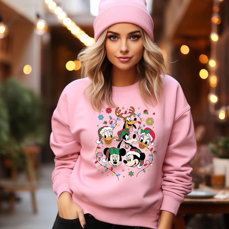 May include: Pink Christmas sweater featuring a festive design with Mickey Mouse, Minnie Mouse, Donald Duck, Goofy, and Pluto. The characters are surrounded by Christmas lights and snowflakes.