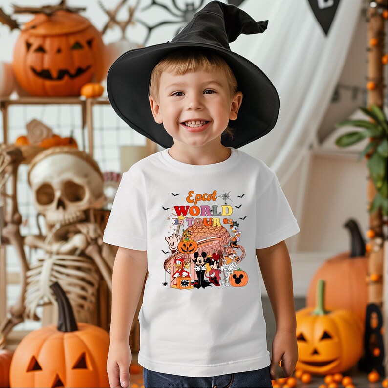 May include: A child wearing a black witch hat and a white t-shirt with the text "Epcot World Tour" and cartoon characters. The background includes Halloween decorations such as pumpkins and a skeleton.