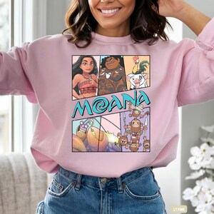 May include: Pink sweatshirt with a cartoon graphic of characters from the movie Moana. The graphic includes Moana, Maui, Pua the pig, Hei Hei the rooster, and the Kakamora.