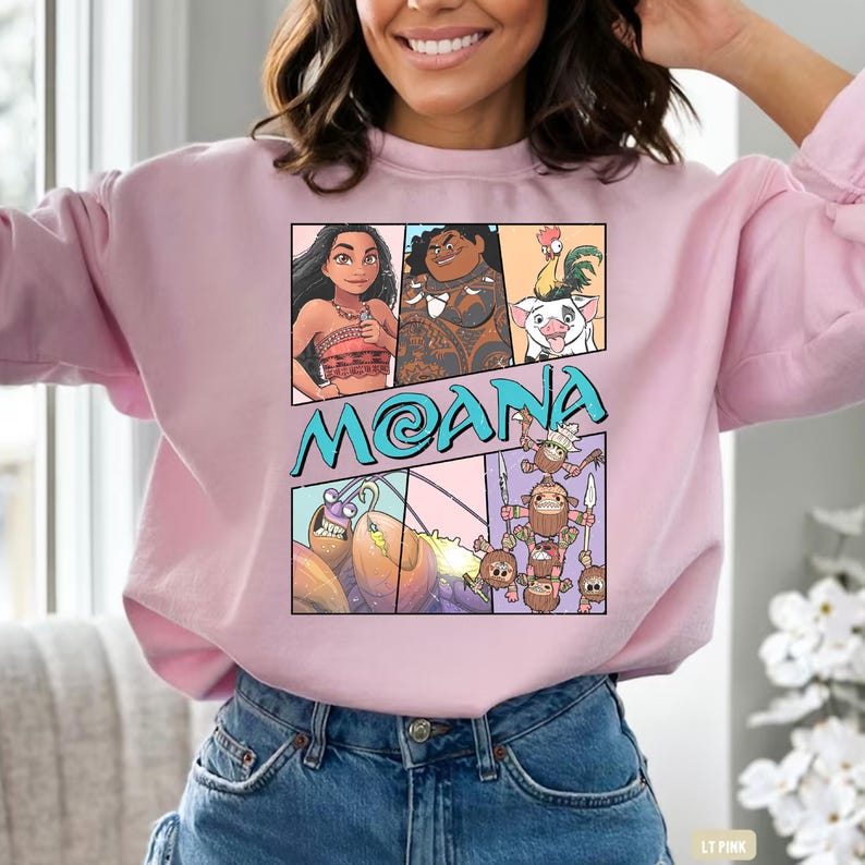 May include: Pink sweatshirt with a cartoon graphic of characters from the movie Moana. The graphic includes Moana, Maui, Pua the pig, Hei Hei the rooster, and the Kakamora.