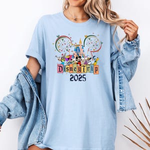 May include: Light blue t-shirt with a graphic of Mickey Mouse and other Disney characters in front of Cinderella's Castle. The text "Disney Trip 2025" is printed below the graphic.