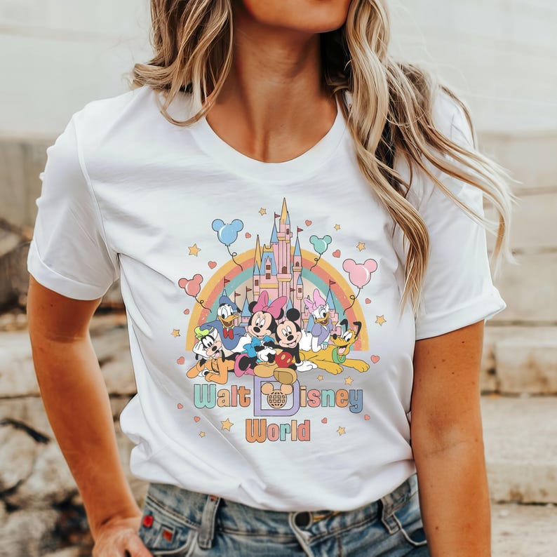 Puede incluir: Camiseta blanca con un gr&aacute;fico colorido de Mickey Mouse y sus amigos frente al Castillo de Cenicienta con un arco&iacute;ris y el texto "Walt Disney World".