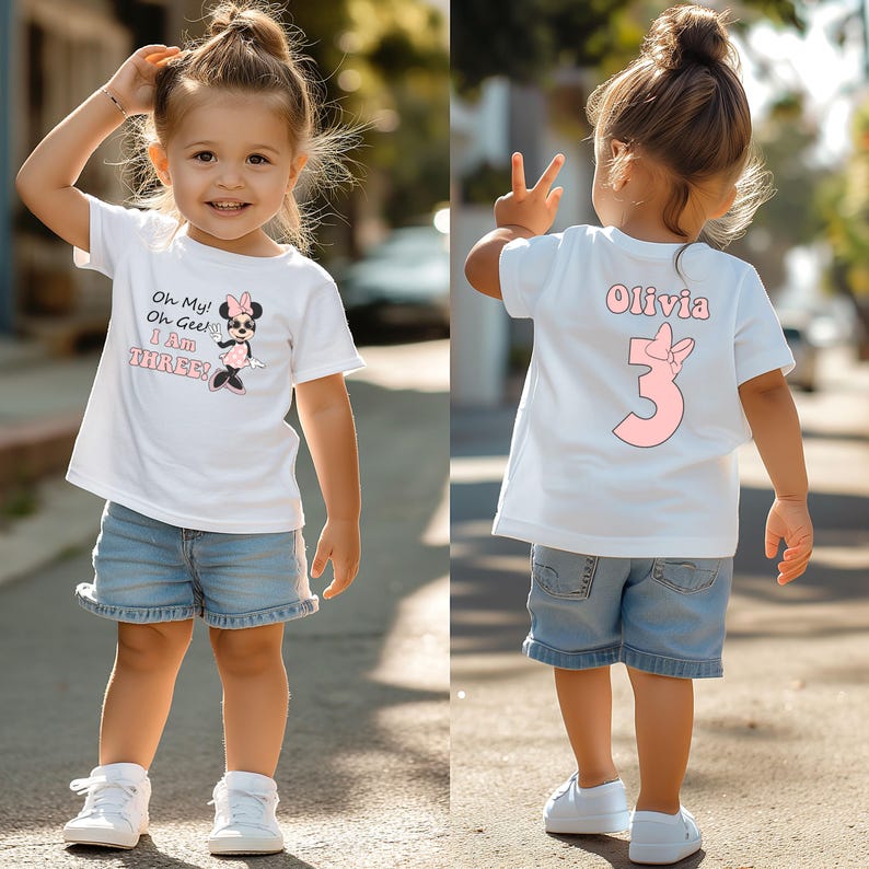 May include: A white t-shirt with a Minnie Mouse graphic and the text "Oh My! Oh Gosh! I Am THREE!" is worn by a young child. The child is also wearing denim shorts and white sneakers. The back of the shirt has the name "Olivia" and the number "3".