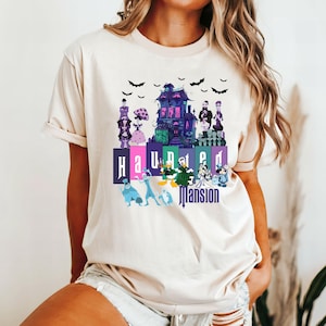 Puede incluir: Una camiseta blanca con un estampado gr&aacute;fico de la atracci&oacute;n Haunted Mansion de Disneyland. El gr&aacute;fico presenta el edificio Haunted Mansion, fantasmas y el texto "Haunted Mansion".