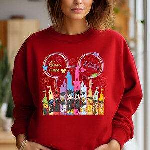 Puede incluir: Sudadera roja con un gr&aacute;fico de Mickey Mouse y otros personajes de Disney frente a un castillo. El gr&aacute;fico tambi&eacute;n incluye el texto "Grad Liam 2025" y las orejas de Mickey Mouse.