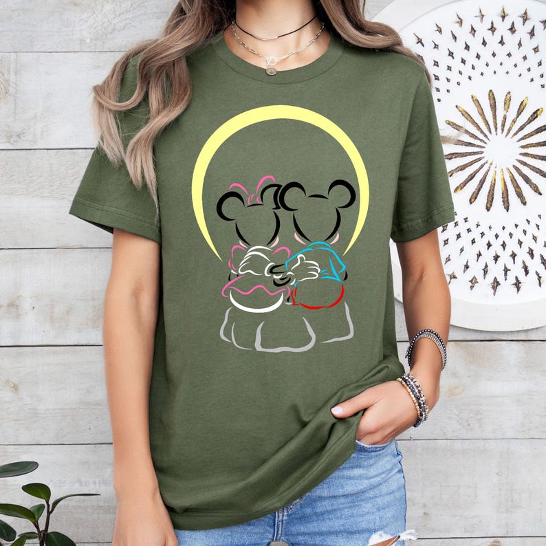 Puede incluir: Camiseta verde oliva con un gr&aacute;fico de dos ratones de dibujos animados abraz&aacute;ndose, sobre un c&iacute;rculo amarillo. Los ratones de dibujos animados est&aacute;n delineados en negro, con acentos rosas, azules y blancos. La camiseta es de cuello redondo y manga corta.