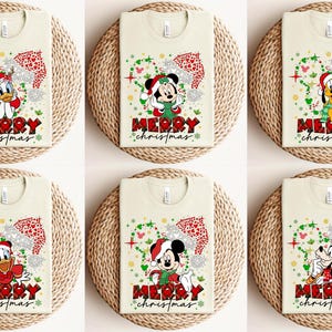 May include: Six beige t-shirts with a Christmas theme featuring Mickey Mouse, Donald Duck, and Goofy. Each shirt has a red and green design with the words "Merry Christmas".