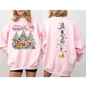 Puede incluir: Sudadera rosa claro con dise&ntilde;o navide&ntilde;o. La parte delantera muestra a Mickey Mouse, el Pato Donald y amigos con el texto "The most Wonderful Time of the year". La parte trasera presenta un dise&ntilde;o vertical de personajes de Disney.