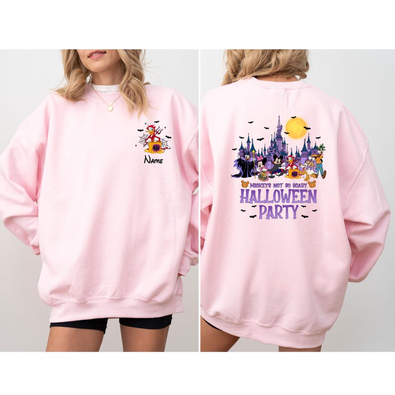 May include: A light pink sweatshirt with a Halloween-themed design. The front features a cartoon character and the word "Name". The back displays a castle, characters, and the text "Mickey's Not So Scary Halloween Party".