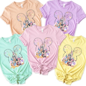 May include: Four t-shirts with a graphic print of Mickey Mouse and friends in front of Cinderella's Castle with fireworks. The shirts are in different colors: peach, lavender, pink, and yellow.