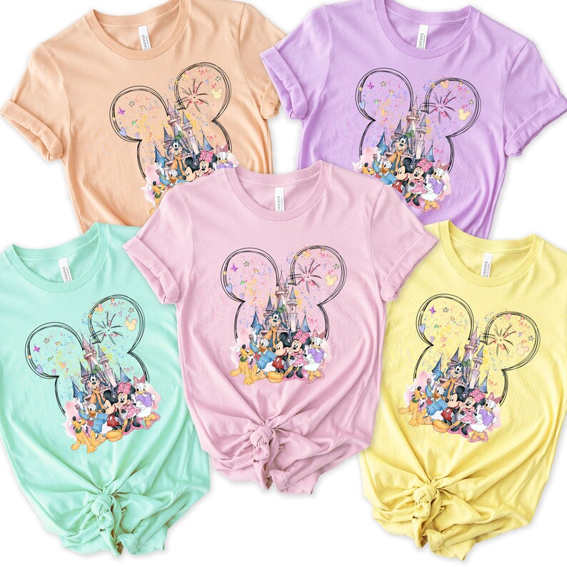 May include: Four t-shirts with a graphic print of Mickey Mouse and friends in front of Cinderella's Castle with fireworks. The shirts are in different colors: peach, lavender, pink, and yellow.