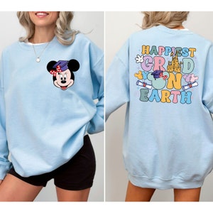 Puede incluir: Sudadera azul claro con un dise&ntilde;o de Mickey Mouse graduado en la parte delantera y el texto "Happiest Grad on Earth" con un dise&ntilde;o de Mickey Mouse graduado en la parte posterior.
