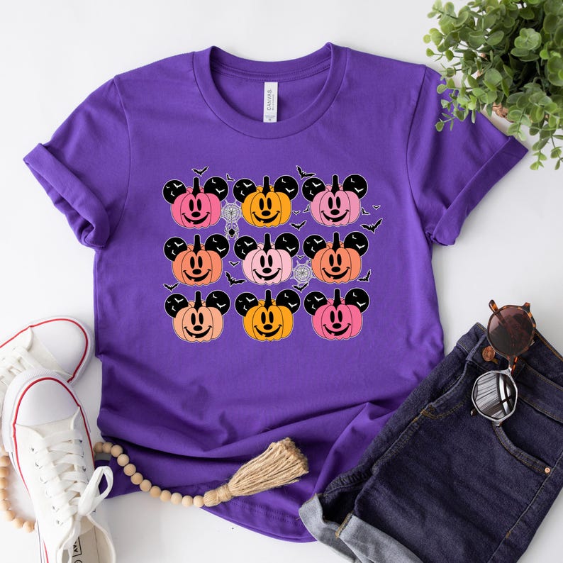 May include: Purple t-shirt with a graphic of multiple orange, pink, and red Mickey Mouse pumpkins with black bats and spiderwebs.