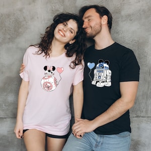 May include: A light pink t-shirt featuring a BB-8 droid design with Minnie Mouse ears and a pink heart balloon. A black t-shirt with an R2-D2 droid design with Mickey Mouse ears and a blue heart balloon.